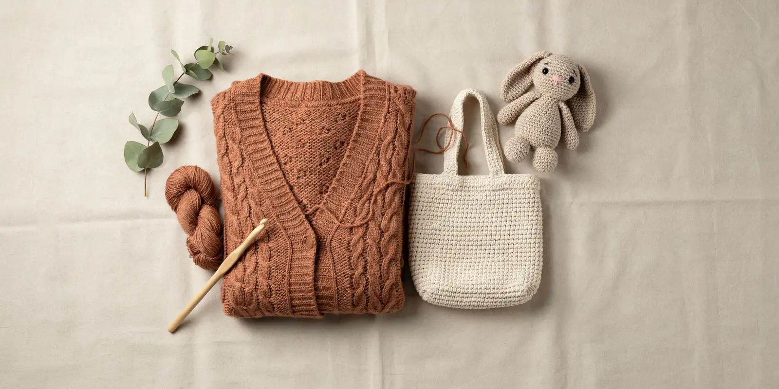 Flat lay of handmade crochet products including a terracotta cardigan, cream tote bag, and amigurumi bunny toy, MapleHookCrochet contact page banner