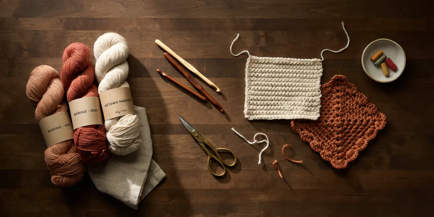 Warm terracotta and cream wool yarn skeins with wooden crochet hooks and hand-crocheted swatches on a rustic wooden table, MapleHookCrochet handmade crochet supplies