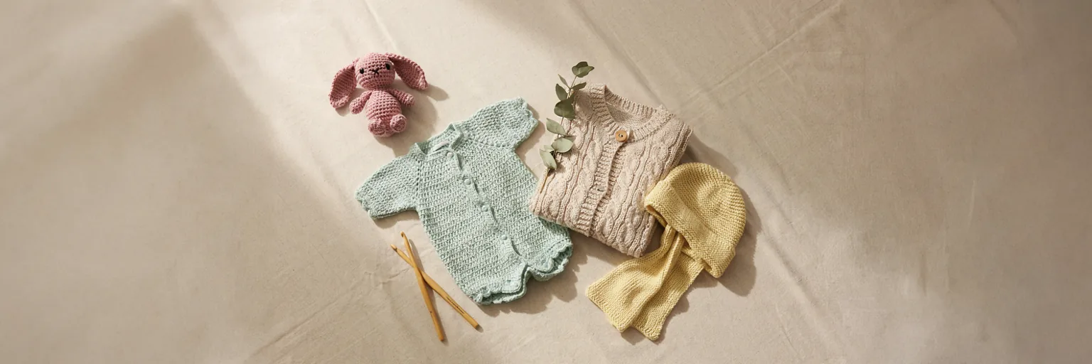 Flat lay collection of handmade crochet items including an amigurumi toy, baby romper, cardigan sweater, and accessories, representing MapleHookCrochet's pattern categories
