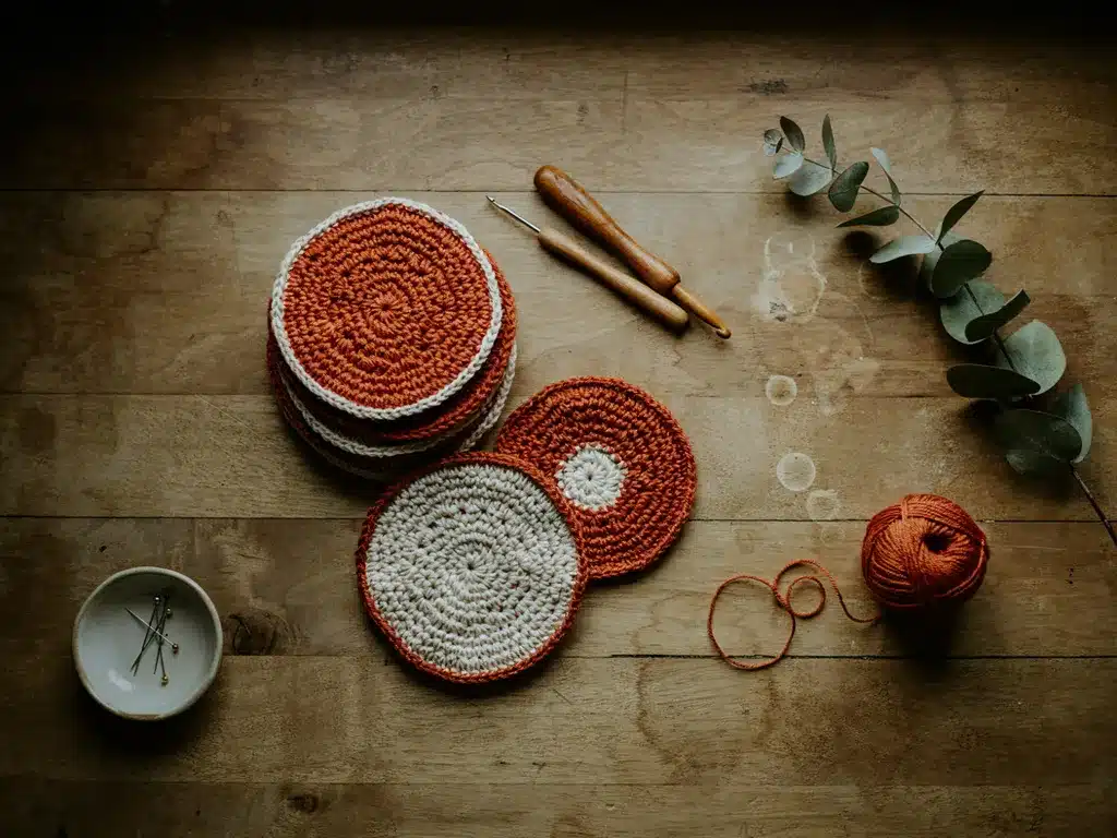 stack of finished single crochet coasters in terracotta and cream yarn on a wooden table